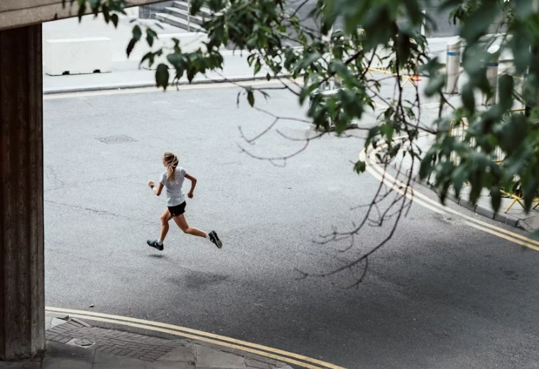 Young blonde woman running in a large city near a tree, showcasi