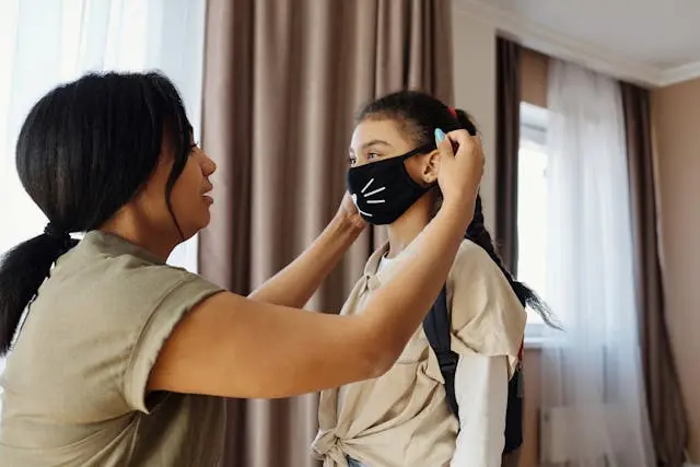 Mother gently putting a child-friendly mask on her daughter, showing care and protection during Covid.